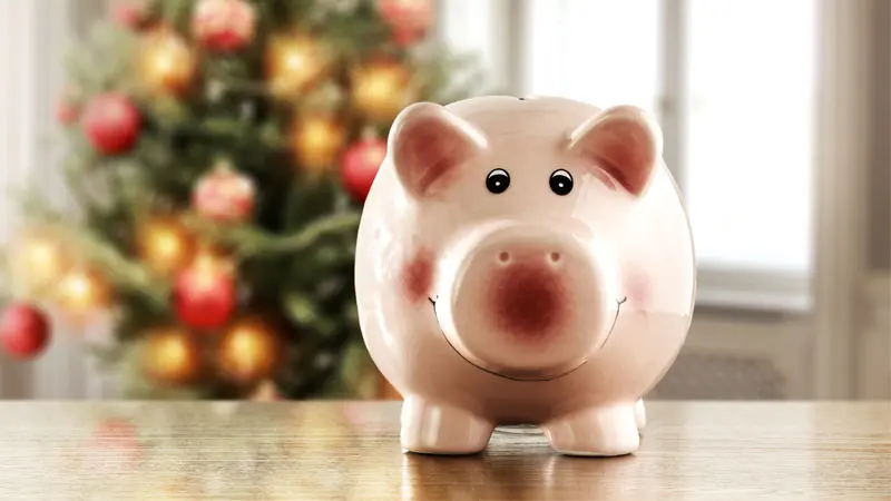 A piggy bank in front of a Christmas tree.