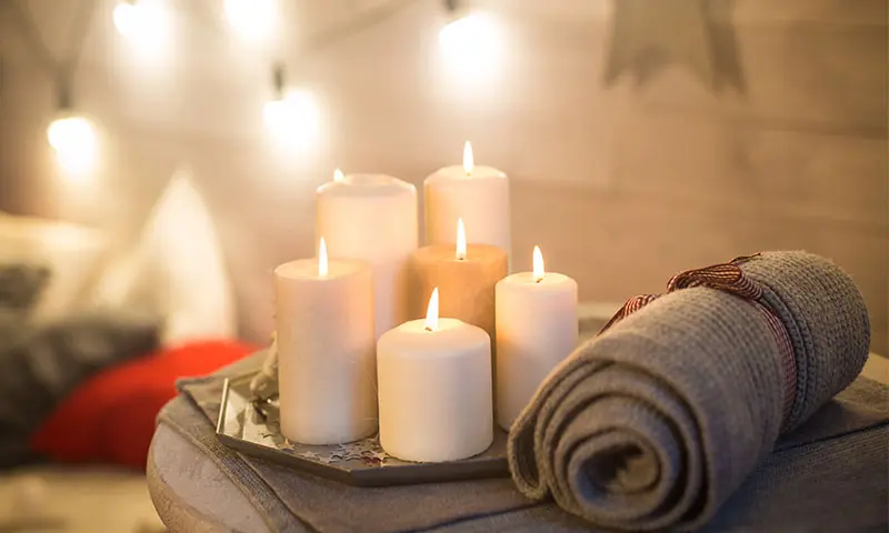 Various candles resting on a side table with a rolled up blanket - perfect decor to make a home feel warm.