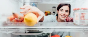 Smiling woman taking a fresh lemon out of the fridge thanks to her home warranty. 