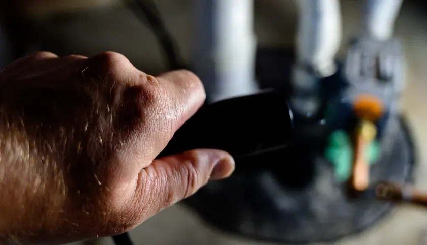 A man holds a flashlight over a sump pump.