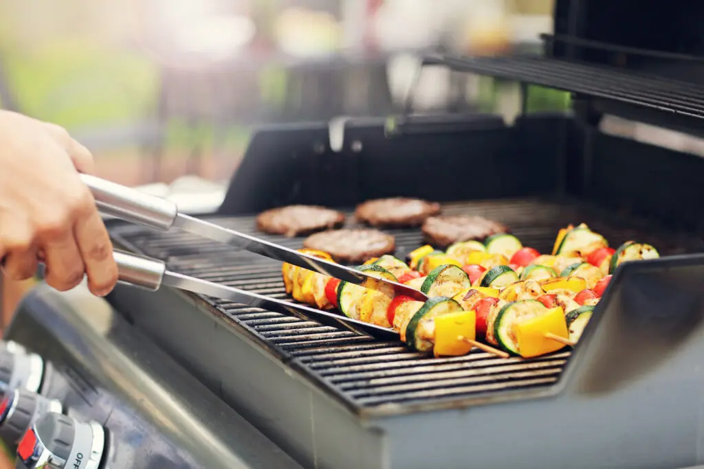 Gas grill with kebabs being flipped using tongs