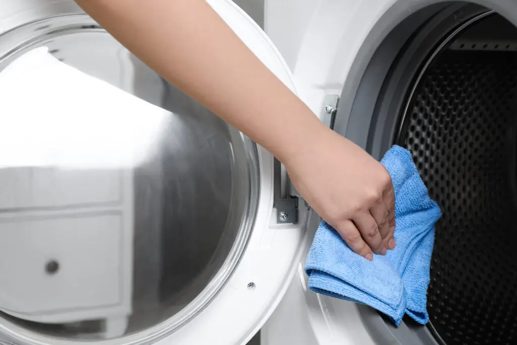 Cleaning inside washing machine with blue microfiber cloth. 